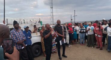 group of people standing outside and listening to someone speaking.
