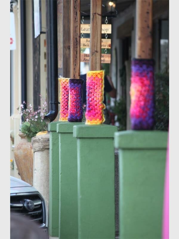 Knitted boots on green pillars outside a shop, vibrant colours and cozy design.