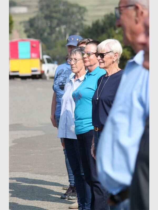Elderly group standing in a line during an outdoor community event.