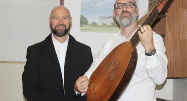 Traditional musician holding lute with presenter at Ridge Times event.
