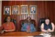 Community leaders seated at a table during a formal meeting in a wood-paneled room.
