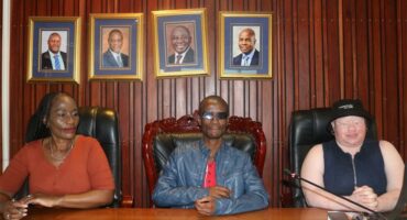 Community leaders seated at a table during a formal meeting in a wood-paneled room.