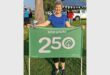 Happy woman holding a green banner with "Secunda 250" at outdoor event.