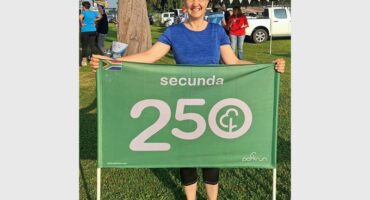 Happy woman holding a green banner with "Secunda 250" at outdoor event.
