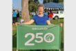 Happy woman holding a green banner with "Secunda 250" at outdoor event.