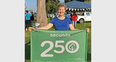 Happy woman holding a green banner with "Secunda 250" at outdoor event.