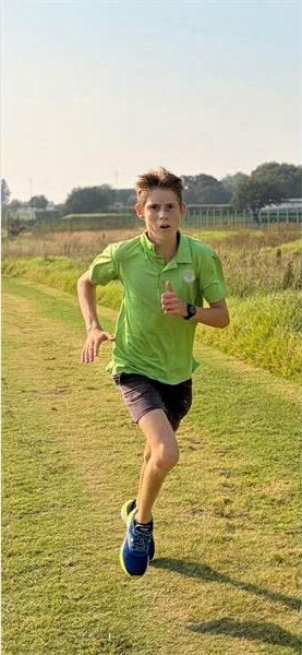 Running boy in green shirt and black shorts on grassy field during daytime.