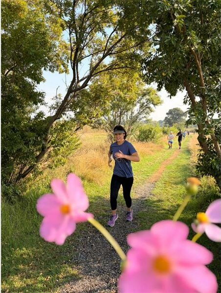 a woman is running in the park. Pink cosmos flowers are in the foreground