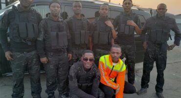 Police officers in tactical gear posing in front of a black vehicle at sunset.