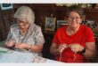 two elderly women knitting at a table