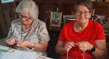 two elderly women knitting at a table