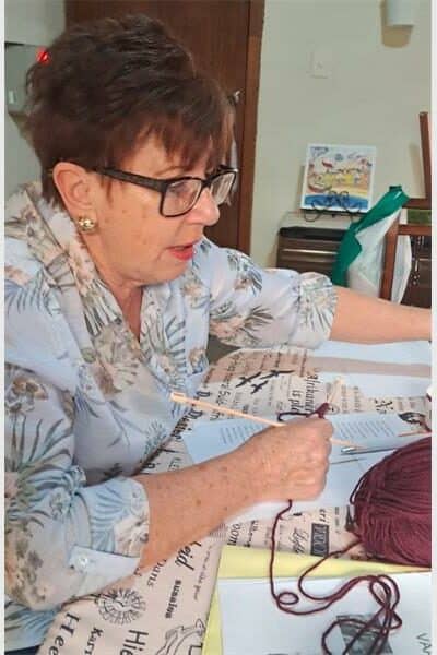 A woman with spectacles are holding knitting pens and wool in her hand