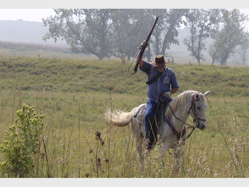 'n perdruiter in die veld hou n vuurwapen omhoog