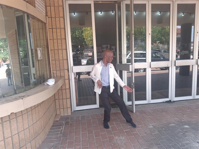 City centre man dancing outside building with glass doors and brick wall.