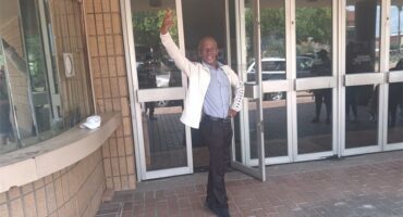 Host waving at the camera outside a building.