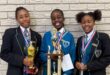 Three girls in school uniforms are holding up trophies