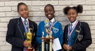 Three girls in school uniforms are holding up trophies