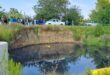 People stand on a verge, looking out onto a pond of water