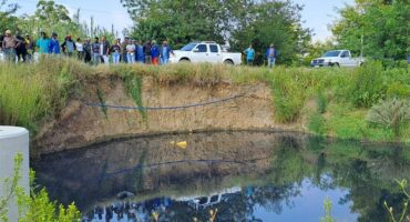 People stand on a verge, looking out onto a pond of water