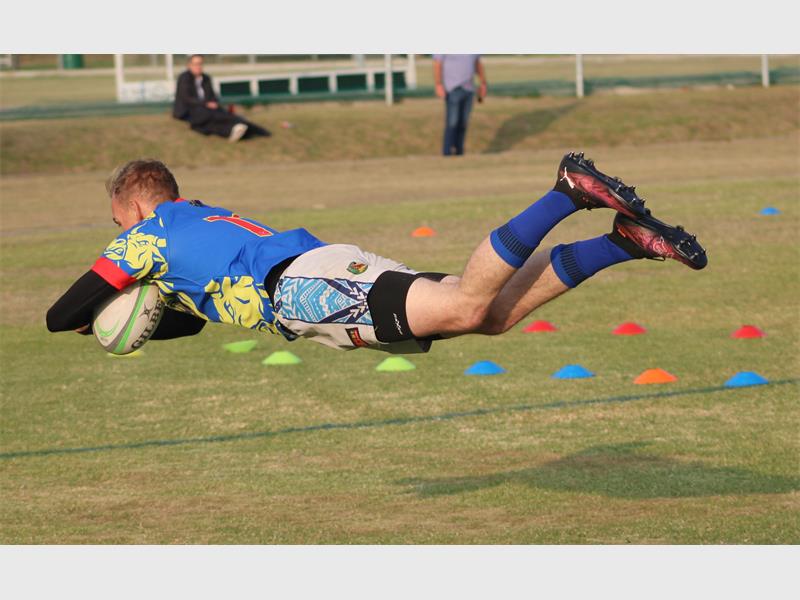 A rugby player in blue runs with the ball while the red team tries to stop him