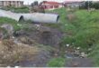 a trench win the field with large sewage pipes in the background