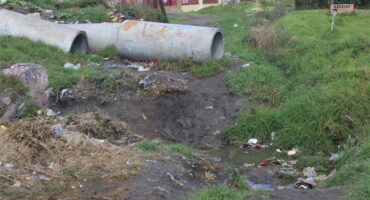 a trench win the field with large sewage pipes in the background