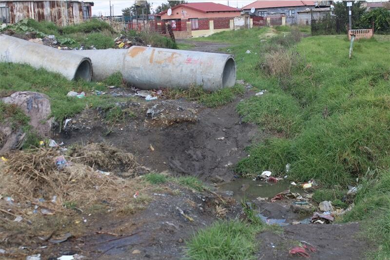 a trench win the field with large sewage pipes in the background