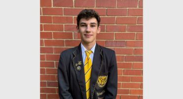 boy in black and yellow school uniform stands in front of a brick wall