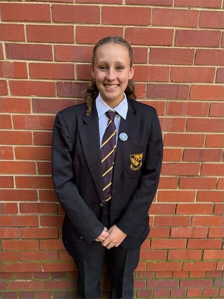 girl in black and yellow school uniform stands in front of a brick wall