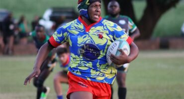 A rugby player with a scrum cap runs with the ball