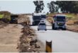Trucks and vehicles drive in opposite lanes to navigate through potholes.
