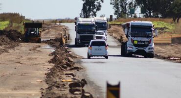 Trucks and vehicles drive in opposite lanes to navigate through potholes.
