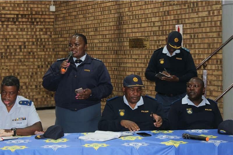A woman in police uniform speaks into a microphone. three other police officers are next to her