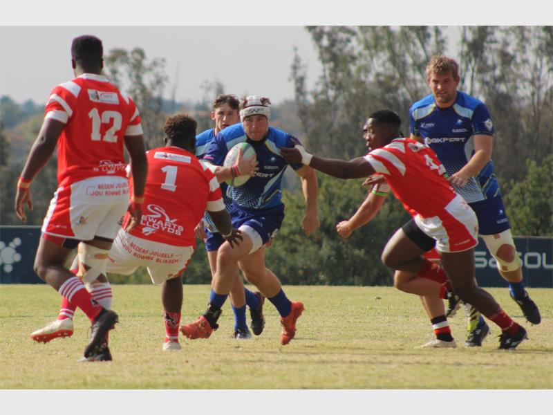 A rugby player in blue runs with the ball while the red team tries to stop him