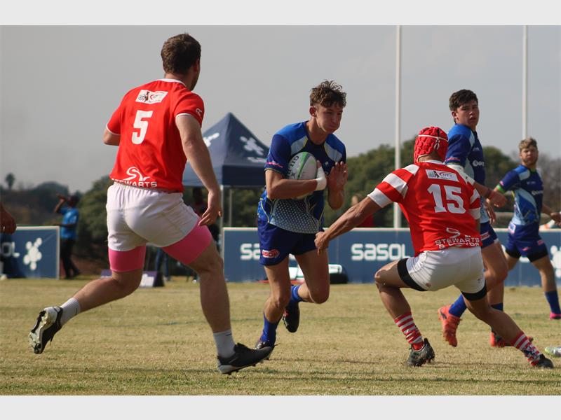 A rugby player in blue runs with the ball while the red team tries to stop him