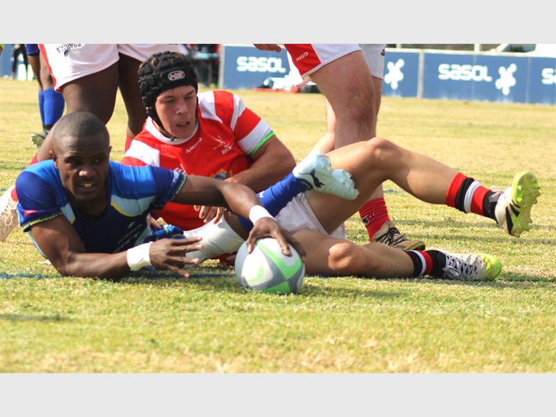 A rugby player in blue scores while the red team tries to stop him