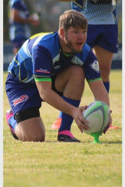 A rugby player in blue aims to kick the ball over the poles