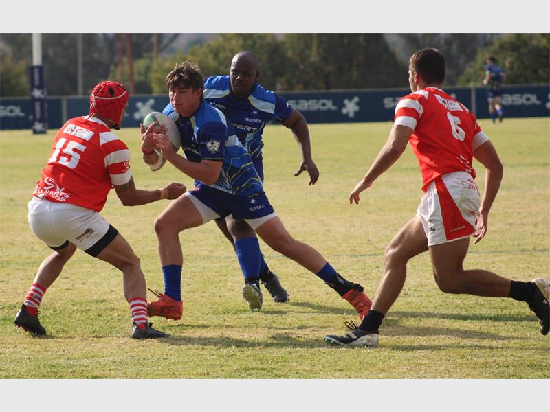A rugby player in blue runs with the ball while the red team tries to stop him