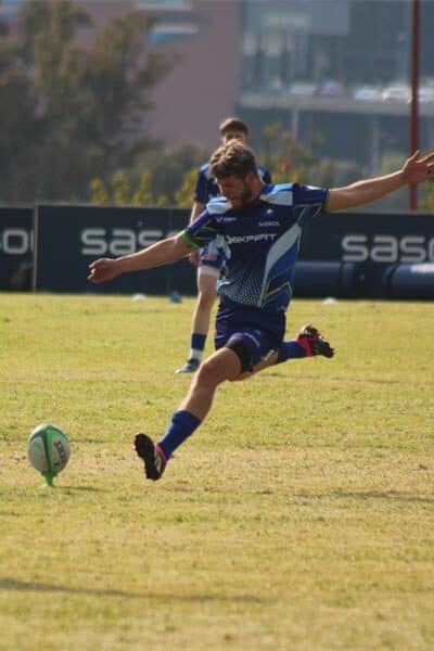 A rugby player in blue aims to kick the ball over the poles