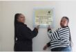 two women point to a plaque on a wall