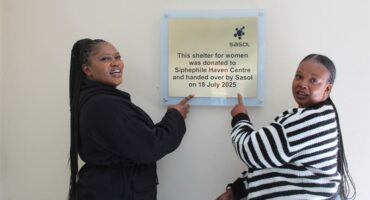 two women point to a plaque on a wall