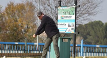 a man wearing a black shirt tees off in golf