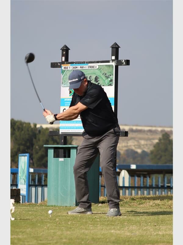 a man wearing a black shirt tees off in golf