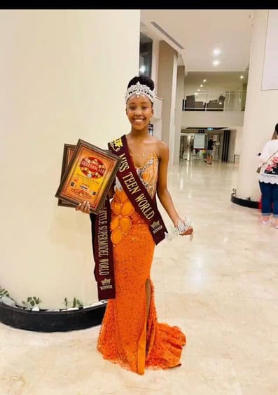 girl in orange dress wearing a crown and holding up 2 certificates