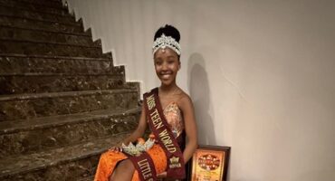girl in orange dress wearing a crown and holding up 2 certificates