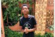 a boy in a black t-shirt and jeans standing in a garden
