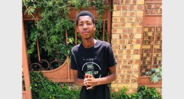 a boy in a black t-shirt and jeans standing in a garden