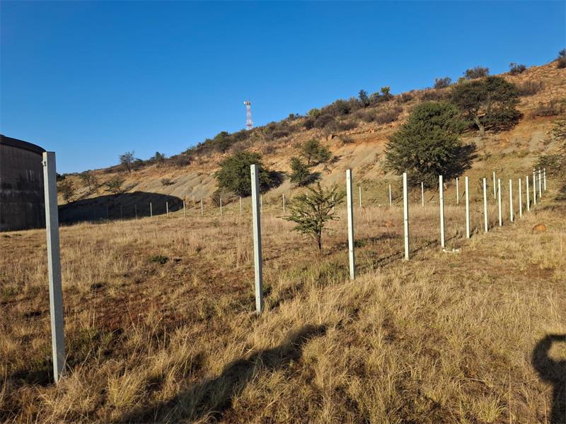 a grassland and hill with fence poles in the foreground