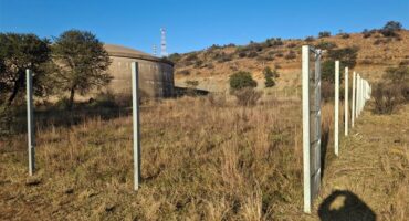 a grassland and hill with fence poles in the foreground