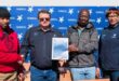 four people with a certificate and school desks